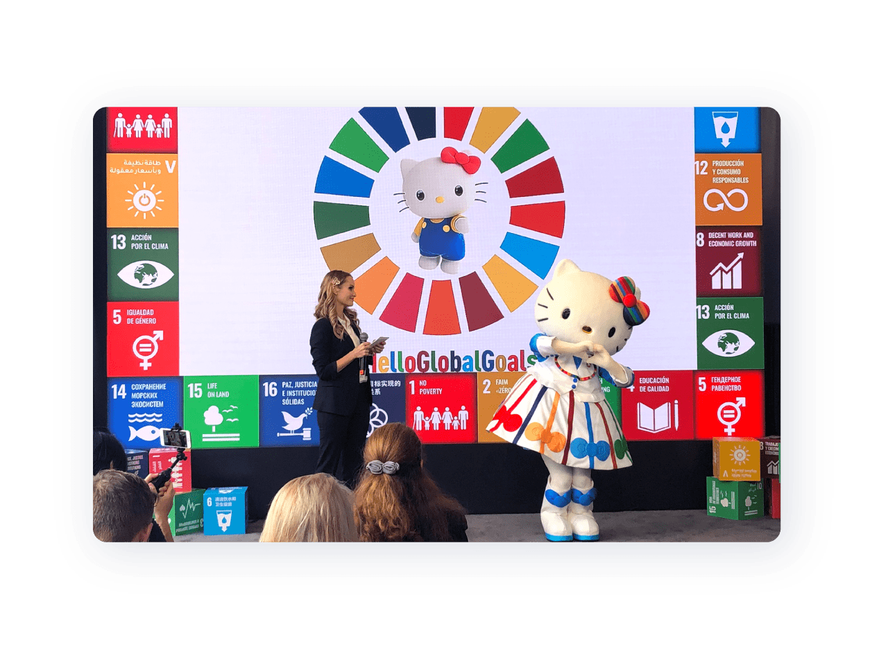 SDGsロゴの表示された画面の前に立つハローキティと女性